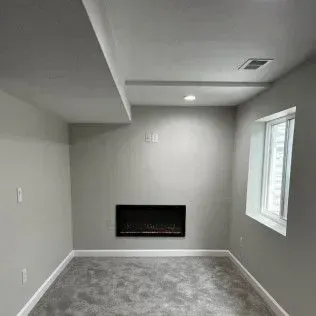 Empty room with fireplace, window, and gray walls, ceiling, and carpet.