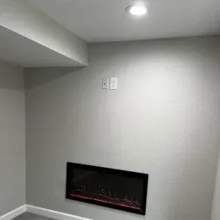 A gray-walled room with a fireplace, recessed ceiling light, and wall-mounted electrical outlets.