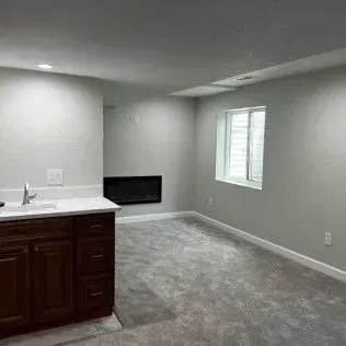 Basement room with wet bar and fireplace, gray carpet, and a window.