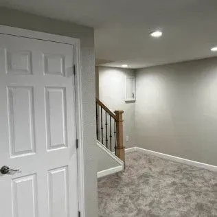 White door, stairs, and carpeted room painted light gray with recessed ceiling lights.