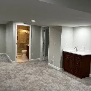 Gray-walled basement with carpet, bathroom visible, and a dark wood vanity with a sink.