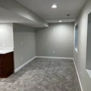 Empty room with gray carpet, walls, and ceiling, with a dark wood cabinet.