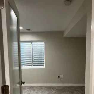 Open doorway leading into a room with a window, gray walls, and carpet.