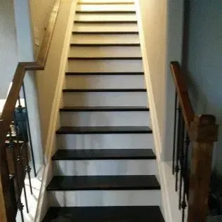 Staircase with white risers and dark treads, wooden handrails, leading upwards.