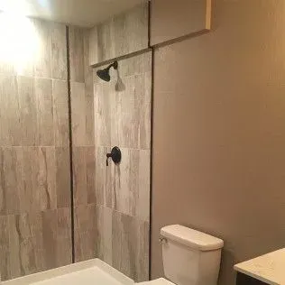 Bathroom with tiled shower, toilet, and light brown wall.