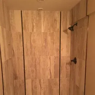 Shower with light brown tiles and black fixtures.
