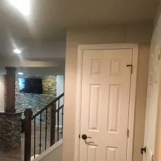 White door in a hallway, with stairs and a TV visible.