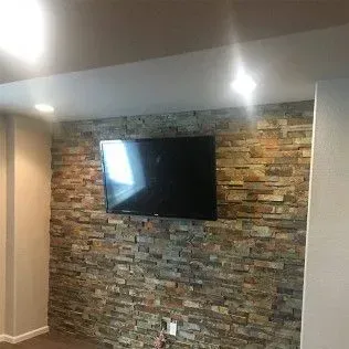 TV mounted on a textured stone wall, beige and brown tones, recessed lighting.