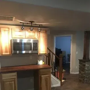 Kitchen with wooden cabinets, microwave, and bar area. A door leads to a staircase.