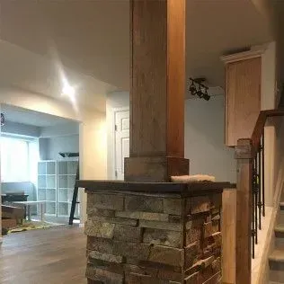 Stone-covered support column with wooden top in a finished basement with a staircase.