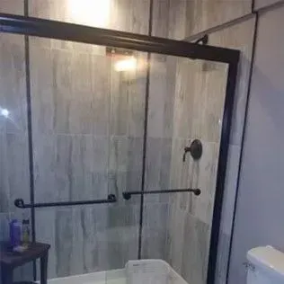 A black-framed glass shower door with a gray tiled wall. Handles are visible.