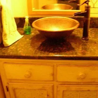 Bathroom sink with copper bowl, black faucet, and cream-colored cabinet.