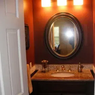 Bathroom with oval mirror, brown walls, and sink with marble countertop.
