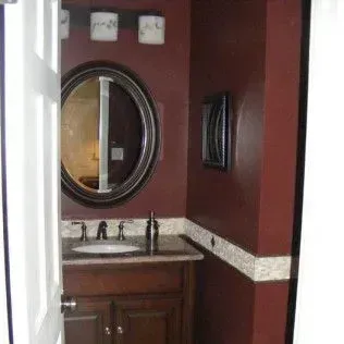 A small bathroom with a burgundy wall, an oval mirror, and a dark wooden vanity.