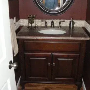 Small bathroom with dark brown vanity, oval mirror, and red walls.