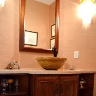 Bathroom with a wooden framed mirror, stone sink, and brown cabinetry. Peach walls and sconce lighting.
