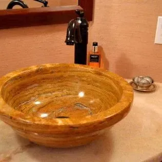 Orange and brown marble vessel sink on a marble countertop with a black faucet.