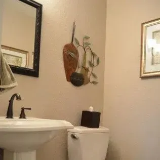 Bathroom interior with sink, toilet, mirror, artwork, and tissue box.