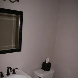 Bathroom with a mirror, sink, and toilet paper dispenser. Gray walls.