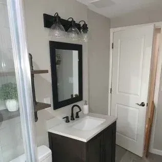 Bathroom with dark wood vanity, black mirror, and three-light fixture above a white sink. White door to the right.