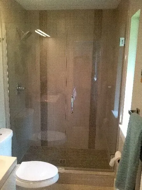 Glass shower enclosure with tile accents and a toilet in a bathroom.