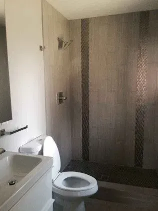 Bathroom with gray tiled shower, toilet, and sink. Dark stripe detail in shower.