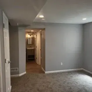 Empty gray bedroom with doorway to bathroom. Gray carpet, white trim.