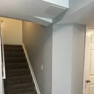 Staircase with brown carpet, gray walls, and a white door leading upstairs.