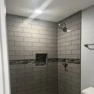 Gray-tiled shower with a niche and decorative border. Includes a showerhead and faucet.