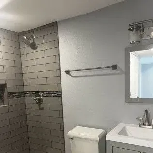 Bathroom with gray tiled shower, toilet, sink, mirror, and towel rack.