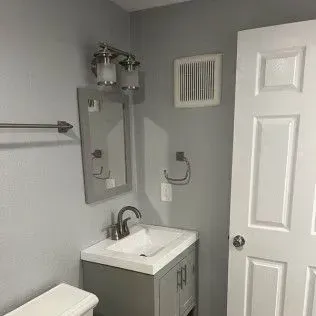 Gray bathroom with vanity, mirror, towel bar, light fixture, and closed white door.