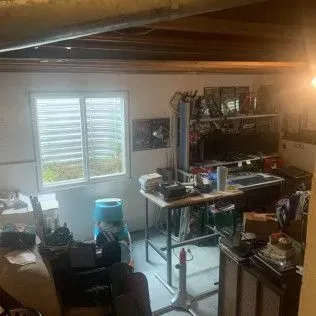 A cluttered basement workspace with a window, desk, and various items.
