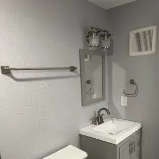 A bathroom with a sink, mirror, and towel rack on a gray wall.