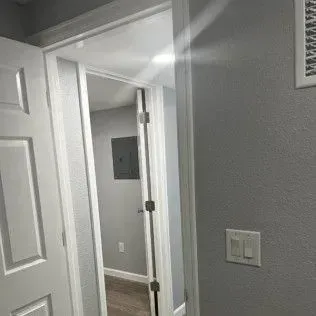 Interior doorway, open to a hallway with a gray electrical panel on the wall. Light shining into the hall.