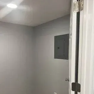 A doorway opening into a small room with a gray wall, light, and electrical panel.