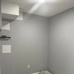 Empty room with gray walls, white ceiling tiles, and a small black shelf.