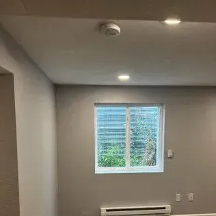 Interior room with a window, white ceiling, smoke detector, and recessed lighting.