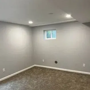 Empty room with gray walls, carpet, and small window.
