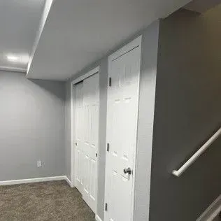 Basement interior with two white doors, gray walls, and a staircase with a white handrail.