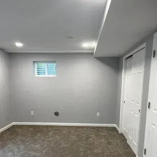 Empty gray room with carpet, recessed lighting, window with shutter, and white closet doors.
