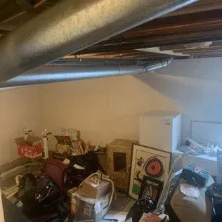 Cluttered basement with ductwork, boxes, and miscellaneous items.