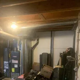 Basement interior with furnace, water heater, ductwork, and cluttered storage area.