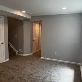 Empty room with gray walls and carpet. Doorways lead to other areas.