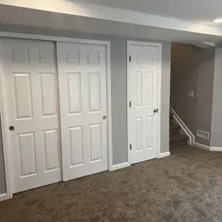 Three white doors in a room with gray walls and carpet. One is a closet with sliding doors, two are hinged.