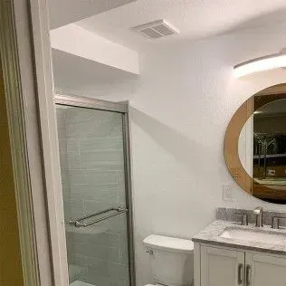 Bathroom interior with a shower, toilet, sink, and mirror. White and beige tones are used.