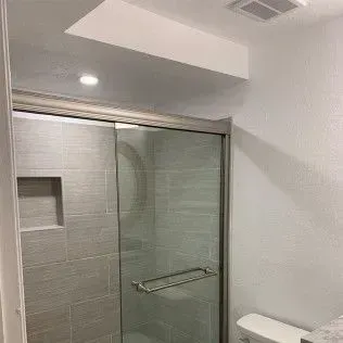 Bathroom with a glass shower door and gray tiled walls.