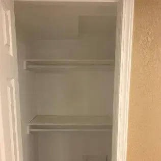 Empty white closet with two shelves and a rod.