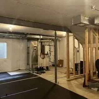 Basement under construction: exposed framing, ductwork, pipes, and support beams.