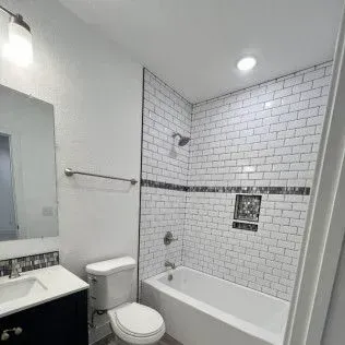 Bathroom with white subway tile, a bathtub, toilet, and sink.