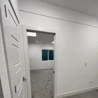 Interior view: Open doorway into a room with a window, white walls, and gray carpet.